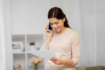 Frau hält Telefon an ihr Ohr und schaut auf Blatt in ihrer Hand